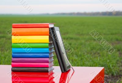 Stack of colorful books and electronic book reader outdoors