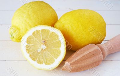 Closeup of three lemons and lemon juicer on white