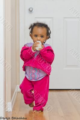 A cute baby girl walking with her bottle