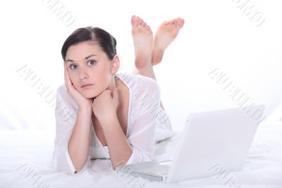 young woman lying down on a bed near a laptop