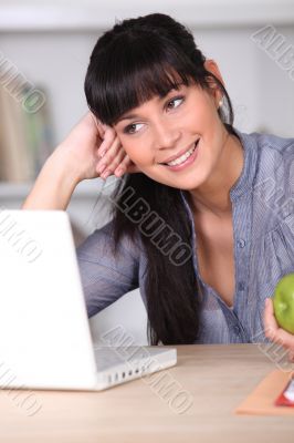Woman working on her laptop and holding an apple Woman working on her laptop and holding an apple