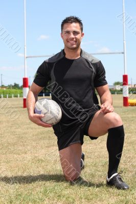 Man on  rugby pitch kneeling with ball under arm