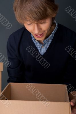 Portrait of young man holding on box against grey wall. 