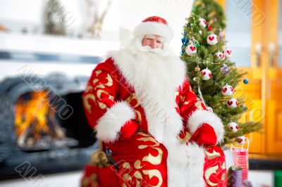 Santa sitting at the Christmas tree, near fireplace.