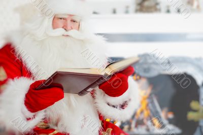 Santa sitting at the Christmas tree, near fireplace and readingÑŽ