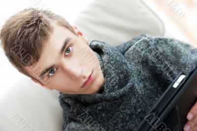 Happy young handsome man at home, smiling and using his tablet computer.