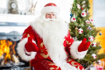 Santa sitting at the Christmas tree, near fireplace and looking.
