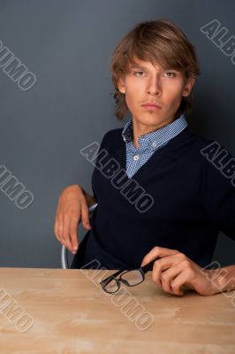 Portrait of young, handsome man thinking while sitting relaxed against grey wall at his office