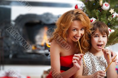 Mother and her daughter sitting together near christmas tree.