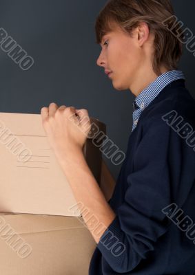 Portrait of young man holding on box against grey wall.