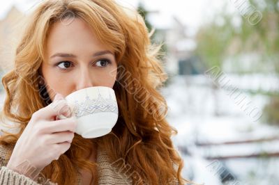 Portrait of beautiful red hair girl drinking coffee on winter background