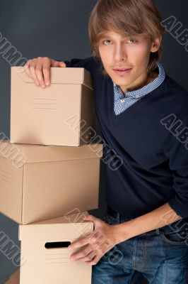 Portrait of young man holding on box against grey wall. He is st