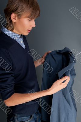 A portrait of a man trying choosing shirts over grey background 