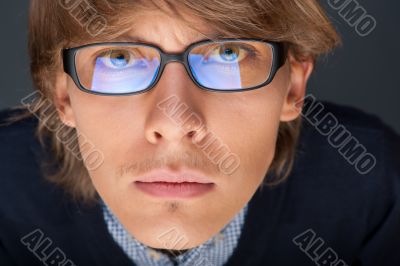 Satisfied young man with glasses looking at camera like at lapto