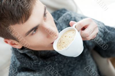 Portrait of a young man drinking coffee while sitting on armchai