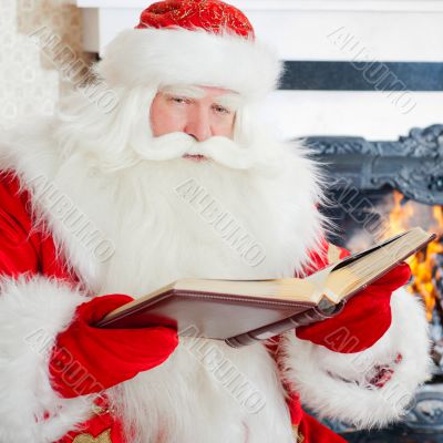 Santa sitting at the Christmas tree, fireplace and reading a boo