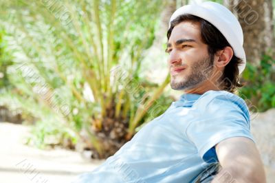 Portrait of a handsome young man sitting in the sun on bench at 