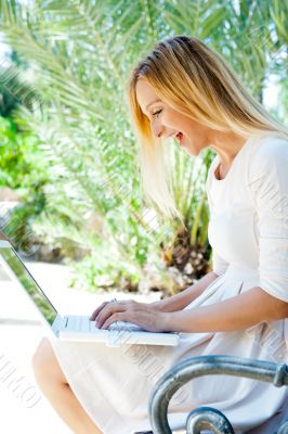 Beautiful woman using laptop while sitting relaxed on bench at s