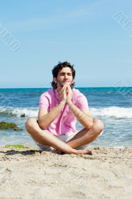 Portrait of young man sitting in lotus pose on sand on beach and