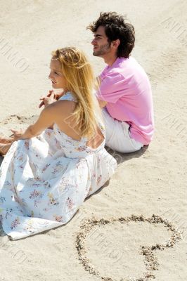 Portrait of young couple sitting together on sand on beach and l