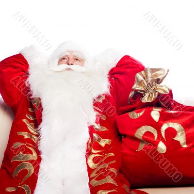 Traditional Santa Claus resting on sofa indoors and daydreaming.