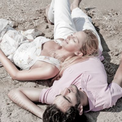 Young couple relaxing on sand at beach and daydreaming with thei