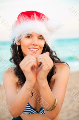Young beautiful woman wearing christmas hat showing heart shape 