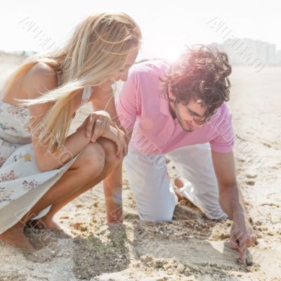 Couple in love drawing a heart in the sand while relaxing at bea