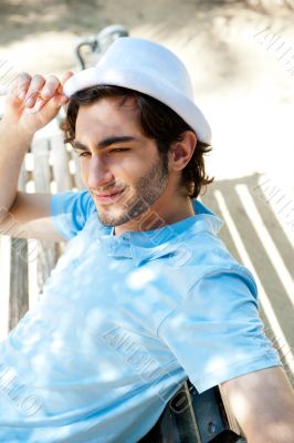 Portrait of a handsome young man sitting in the sun on bench at 