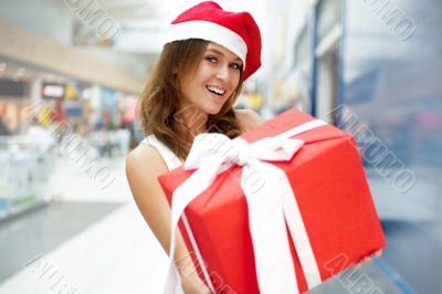 Young happy girl in Christmas hat. Standing indoors and holding 