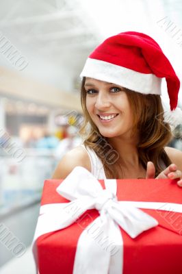 Young happy girl in Christmas hat. Standing indoors and holding 