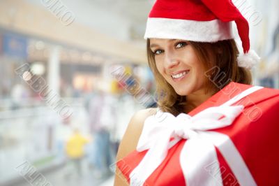 Young happy girl in Christmas hat. Standing indoors and holding 