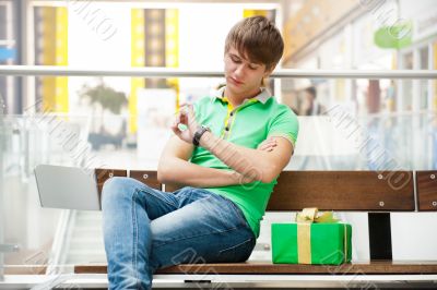 Portrait of young man inside shopping mall with gift box sitting
