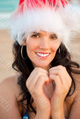 Young beautiful woman wearing christmas hat showing heart shape 