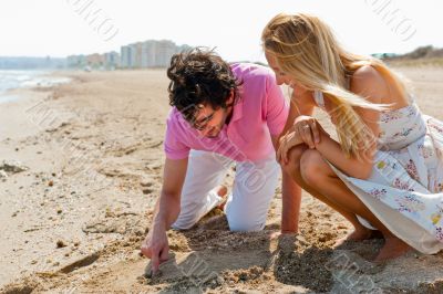 Couple in love drawing a heart in the sand while relaxing at bea