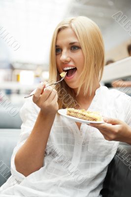 Portrait of young pretty smiling woman eating cake at shopping m