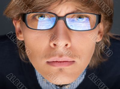Satisfied young man with glasses looking at camera like at lapto