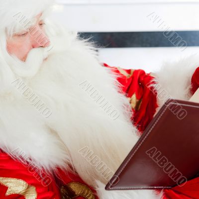 Santa sitting at the Christmas tree, fireplace and reading a boo