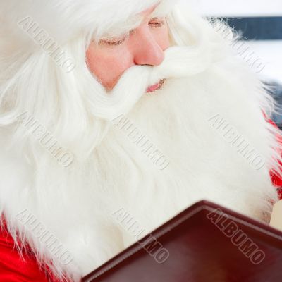 Santa sitting at the Christmas tree, fireplace and reading a boo
