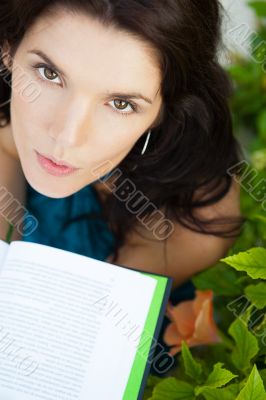 Beautiful girl sitting at park and reads the book. Looking up at