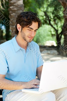 Portrait of a young man with laptop outdoor sitting on bench