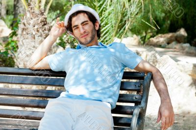 Portrait of a handsome young man sitting in the sun on bench at 