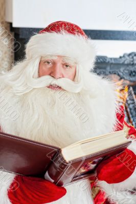Santa sitting at the Christmas tree, fireplace and reading a boo