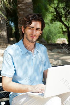 Portrait of a young man with laptop outdoor sitting on bench