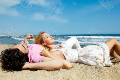 Young couple lying together on a sand by sea and looking to a sk