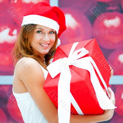 Young happy girl in Christmas hat. Standing indoors and holding 