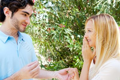 Happy young hispanic man gifting a ring to a beautiful surprised