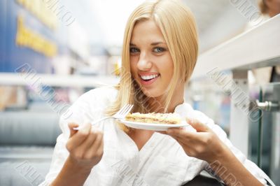Portrait of young pretty smiling woman eating cake at shopping m
