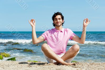 Portrait of young man sitting in lotus pose on sand on beach and