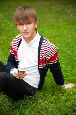 Student outside sitting on grass and holding digital gadget 